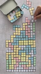 main d'un enfant jouant à tetris en papier dans une petite boite en fer